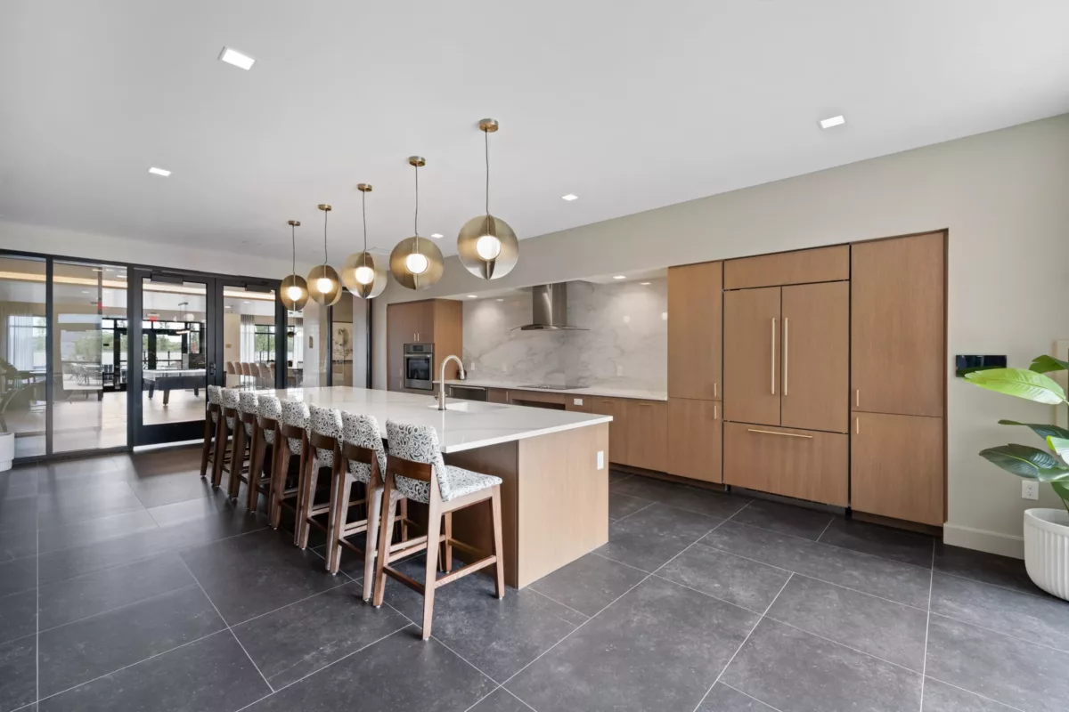 Large kitchen with wood cabinetry, marble backsplash, long island, bar stools, and pendant lights.