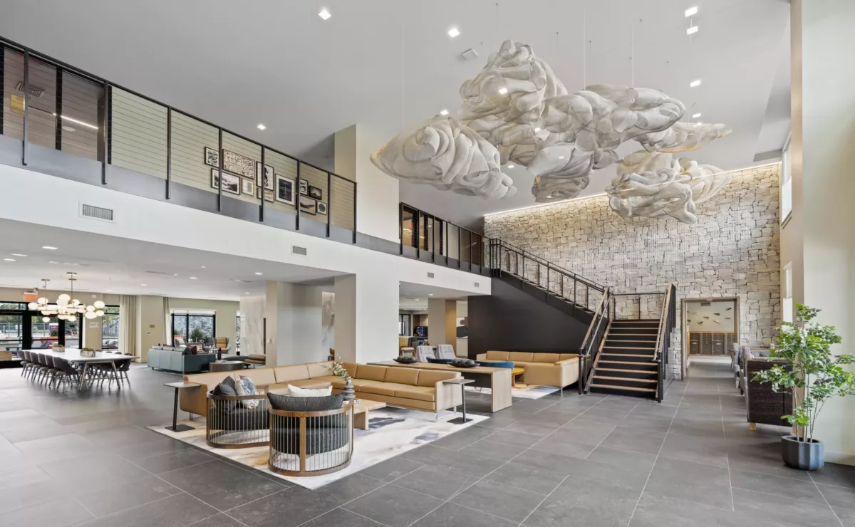 Lobby with a large open space, lounge seating, and a staircase against a textured stone wall.