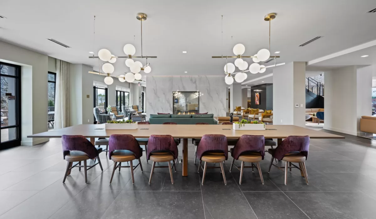 Seating area with a long wood table, maroon chairs, modern light fixtures, and a marble accent wall.