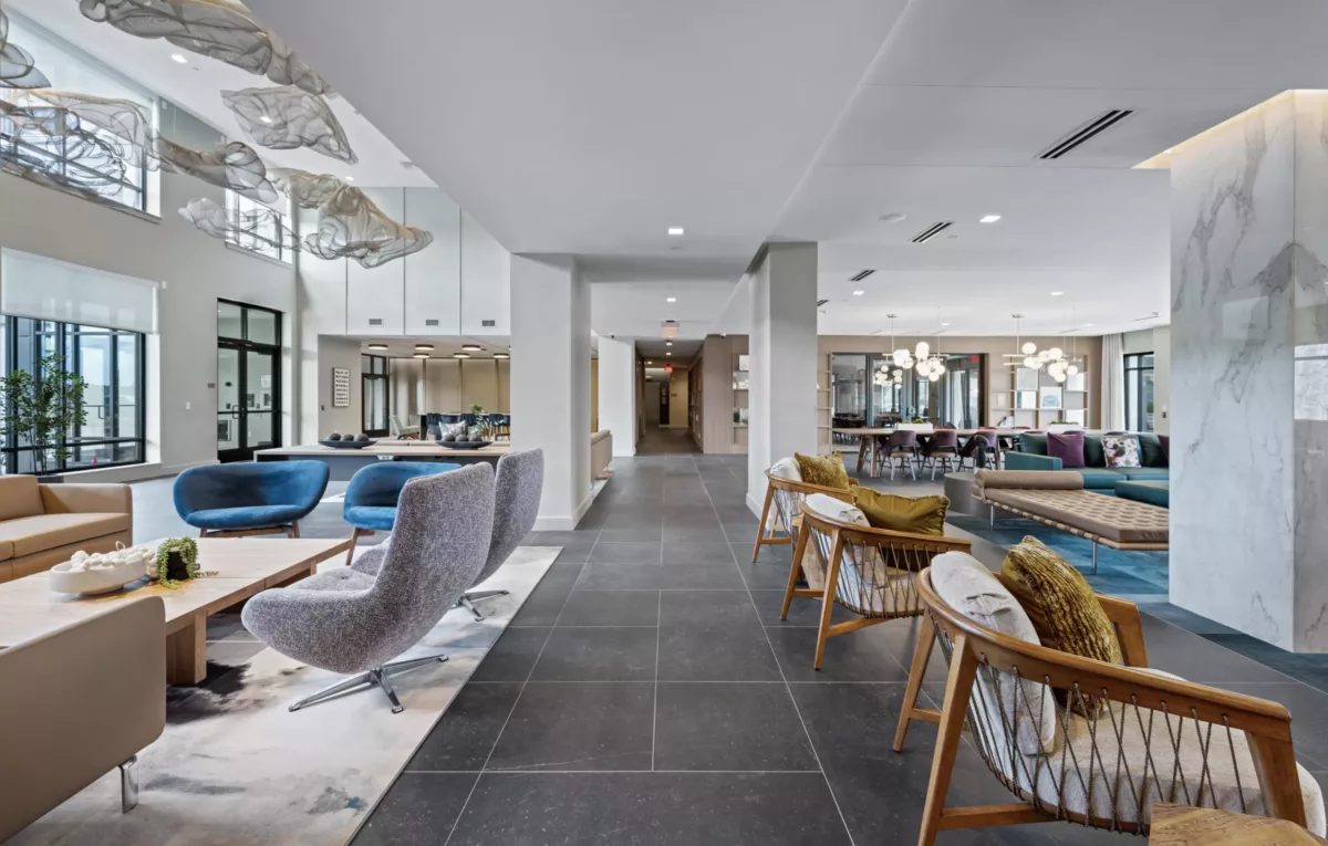 Lounge with grey and blue chairs, art fixtures on the ceiling, and glass doors leading to outside.