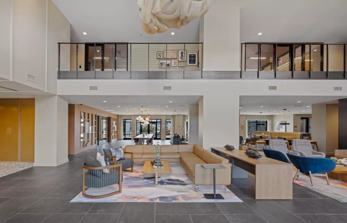 Open lounge area with beige sectional sofa, blue chairs, and upstairs loft with framed artwork.