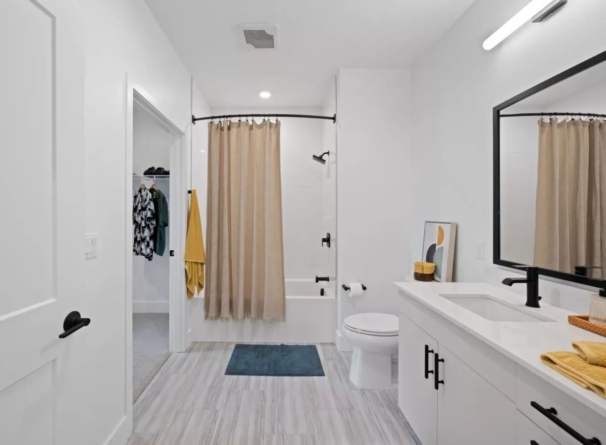 Modern bathroom with a bathtub, beige shower curtain, white vanity, and a closet visible through an open door.