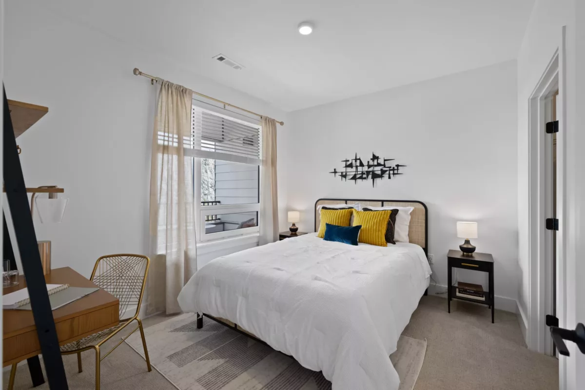 Bedroom with white bedding, yellow pillows, a desk, and metal decor on the wall.