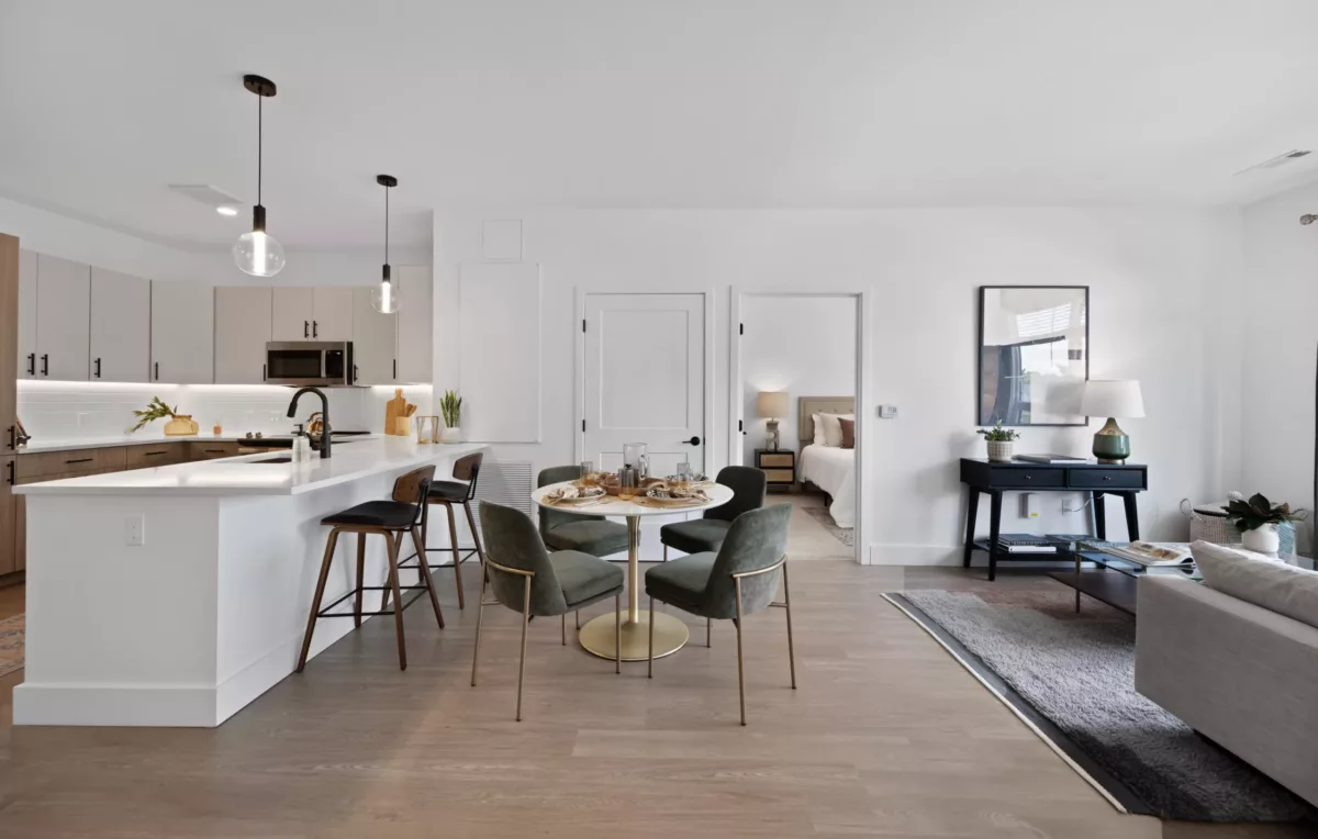 Dining area with round table and dark green chairs, next to the kitchen counter with high stools.