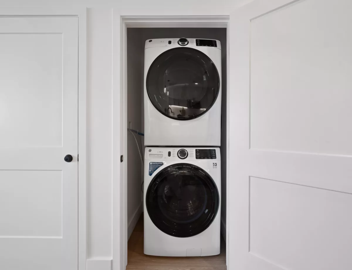 Compact laundry closet with stacked white washer and dryer units behind partially open doors.