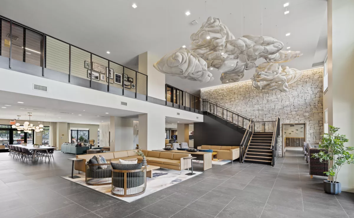 Lobby with a large open space, lounge seating, and a staircase against a textured stone wall.