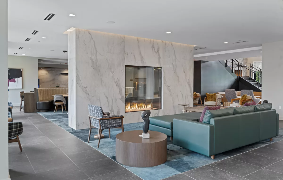 Seating area with teal couch, chairs, a marble wall with a glass fireplace, and modern decor.
