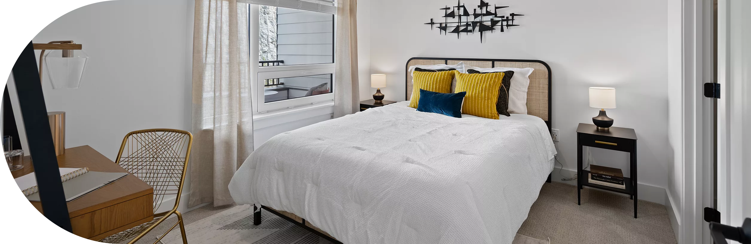 Bright bedroom with white bedding, gold accents, and a desk near the window.